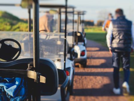 The image shows several golf carts parked on a path with people walking nearby.