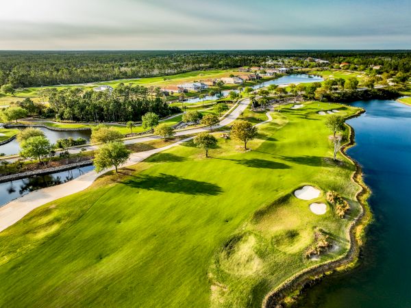 The image shows an aerial view of a lush golf course with sand traps, water features, and surrounding greenery.