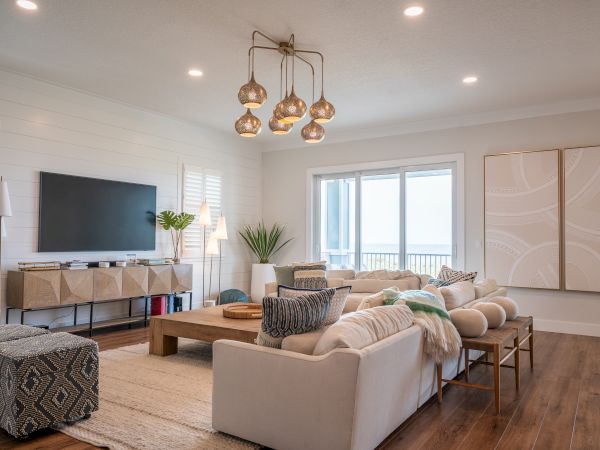 A modern living room with a sectional sofa, wall TV, pendant lights, framed art, and bright ocean-view windows, welcoming and stylish.