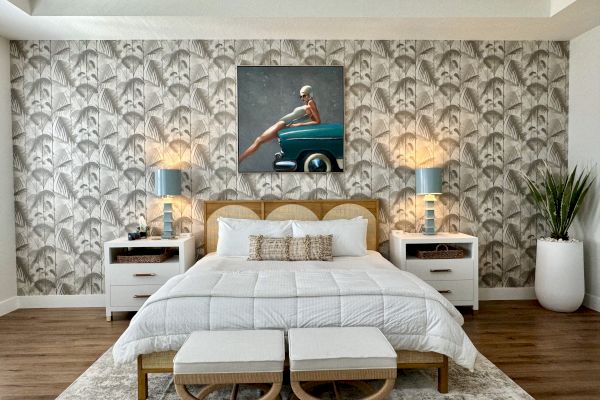 A stylish bedroom with patterned wallpaper, a bed with white linens, two lamps on side tables, and a plant in a pot.