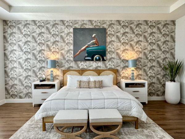 A stylish bedroom with patterned wallpaper, a bed with white linens, two lamps on side tables, and a plant in a pot.