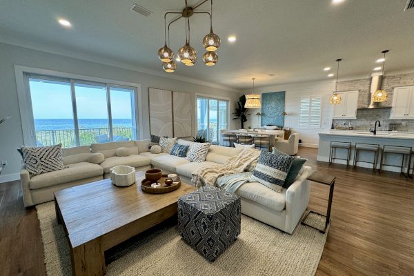 A modern living room with a sea view, featuring a large sectional sofa, wooden coffee table, and open kitchen with a dining area.