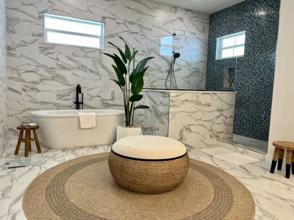 A modern bathroom with a freestanding tub, a plant, mosaic-tiled shower, and round rug, creating a stylish, serene atmosphere.