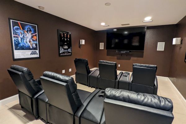A home theater with six black recliners, wall-mounted screen, and movie posters on brown walls.