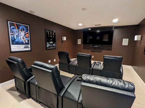 A home theater with six black recliners, wall-mounted screen, and movie posters on brown walls.