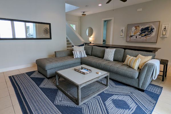 A modern living room with a grey sectional sofa, patterned rug, coffee table, wall art, and ceiling fan, creating a cozy atmosphere.