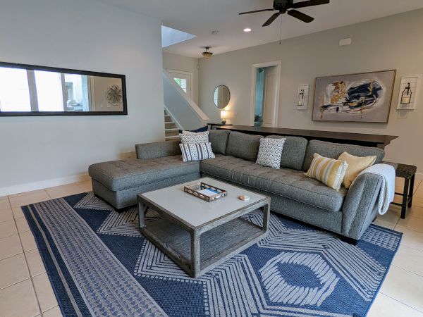 A modern living room with a grey sectional sofa, patterned rug, coffee table, wall art, and ceiling fan, creating a cozy atmosphere.