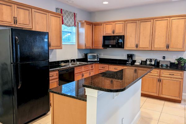 A kitchen with wooden cabinets, black countertops, black appliances, and a kitchen island. Various kitchen gadgets are on the counter.