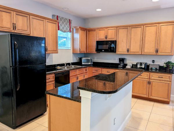 A kitchen with wooden cabinets, black countertops, black appliances, and a kitchen island. Various kitchen gadgets are on the counter.