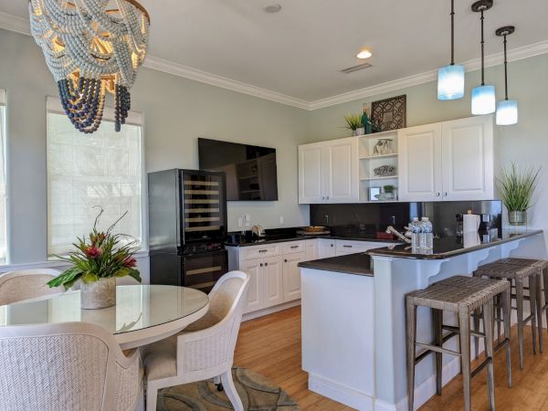 A modern kitchen with white cabinets, bar stools, and a round dining table. A beaded chandelier hangs above the table.