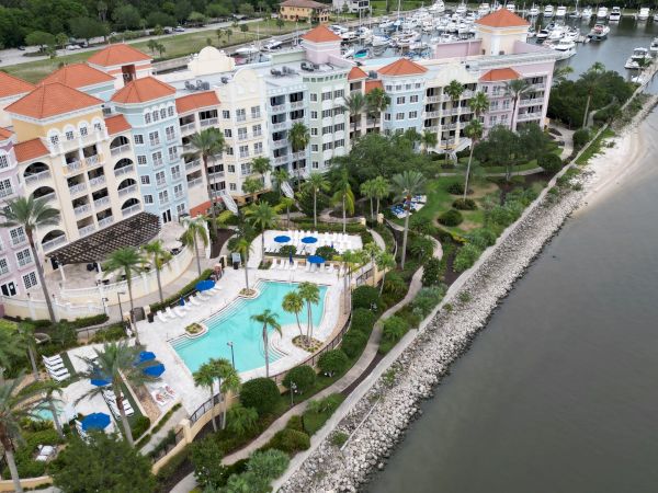 Aerial view of a waterfront resort with colorful buildings, a pool, lush gardens, and a marina with boats docked along the shore.