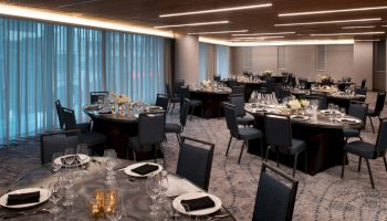 The image shows an elegant dining area with round tables, chairs, black napkins, and dim lighting, suggesting a formal or banquet setting.