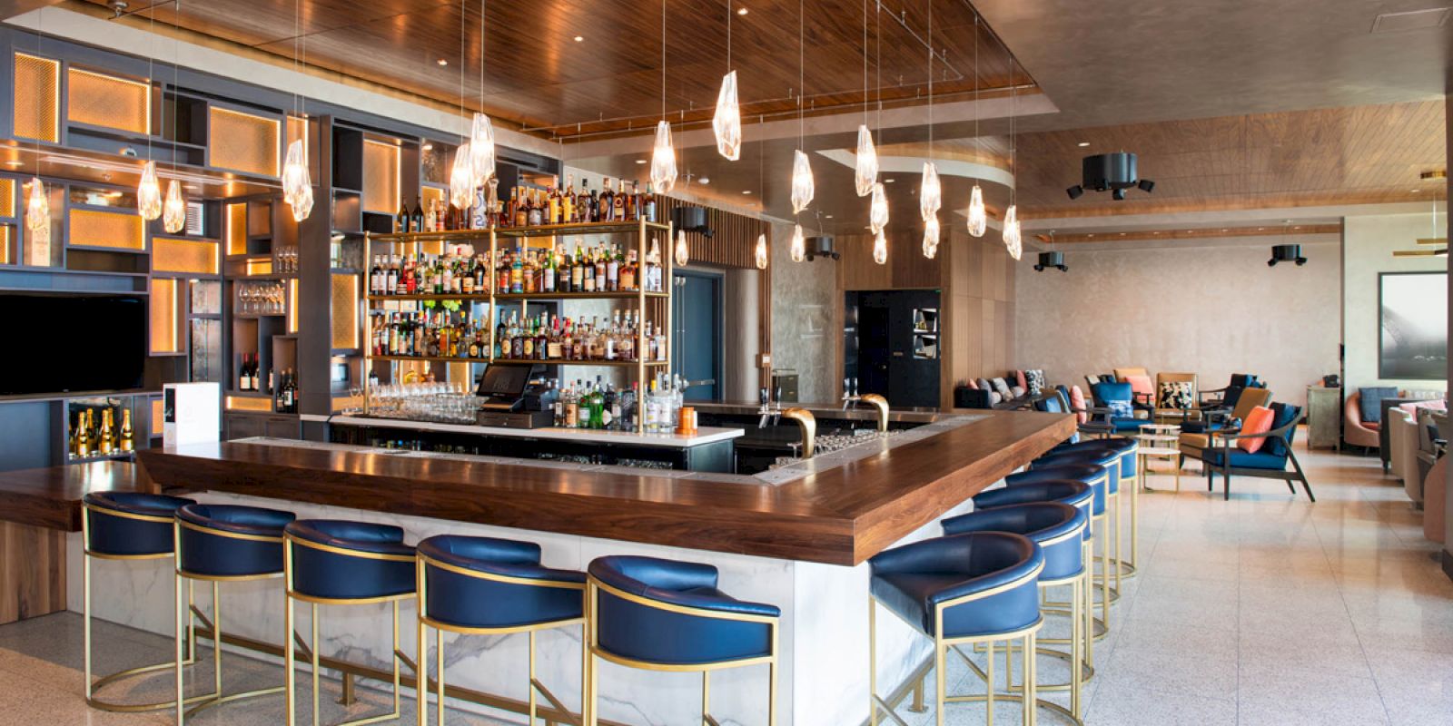 A modern bar with blue chairs, hanging lights, and a fully stocked back bar. The space appears spacious and stylish.