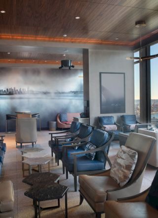A modern lounge with plush seating, large windows offering a waterfront view, and a cityscape mural on the wall.
