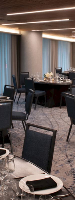 An elegantly set dining room with round tables, dark chairs, white flowers, and dim lighting, creating a sophisticated atmosphere.