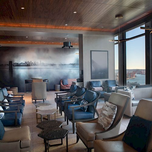 A modern lounge with comfortable seating, large windows with a view of the city and water, and a mural on the wall, creates a cozy vibe.