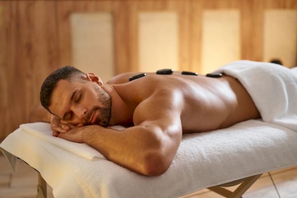 A man is lying face down on a massage table with hot stones placed on his back, creating a relaxing spa atmosphere.