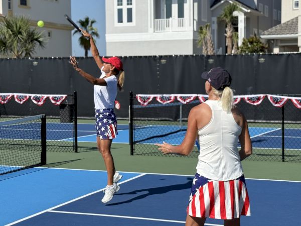 Two women playing tennis on an outdoor court, both wearing patriotic-themed outfits and hats.
